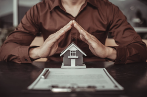 Graphic of an insurance salesman with hands placed atop a model home